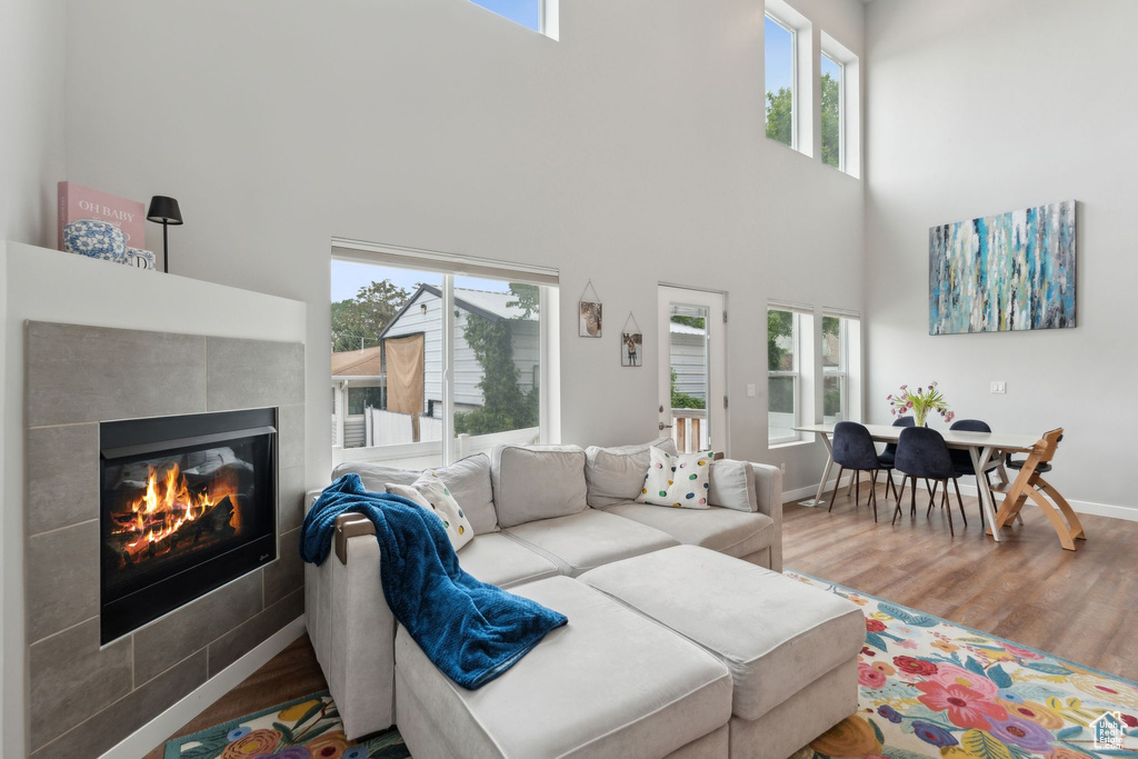 Living area featuring wood finished floors, a towering ceiling, a tile fireplace, and baseboards