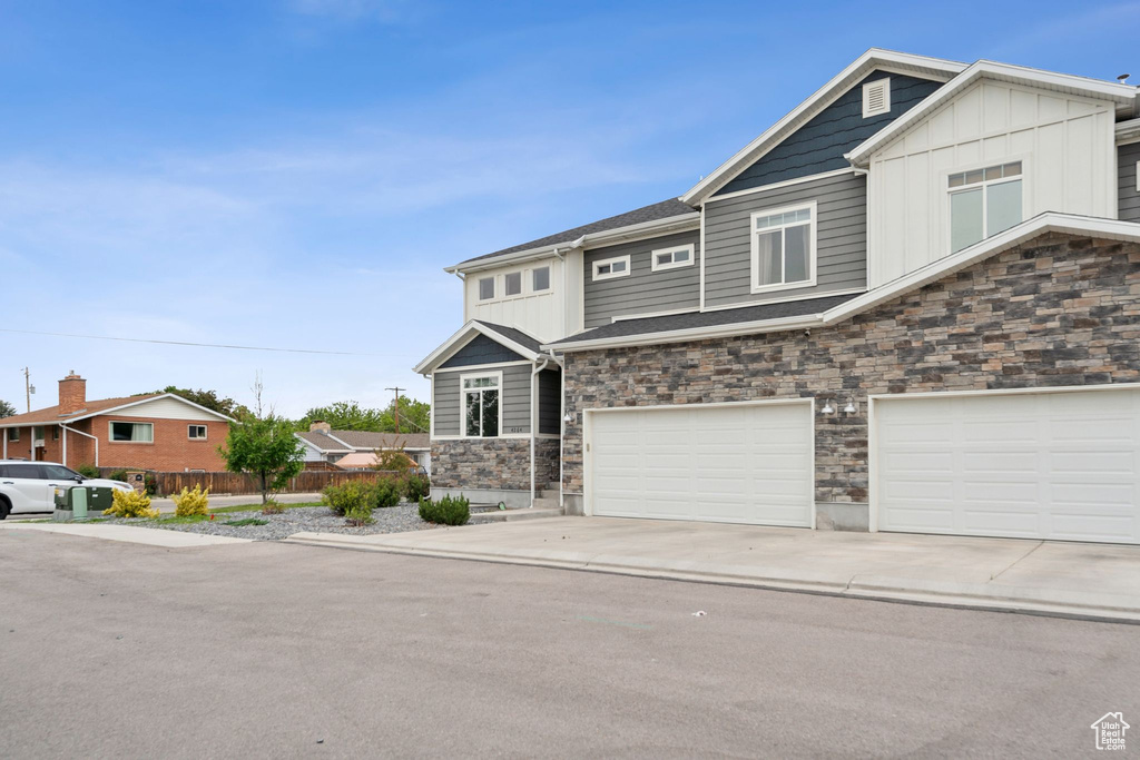 View of front facade with stone siding, board and batten siding, a garage, and driveway