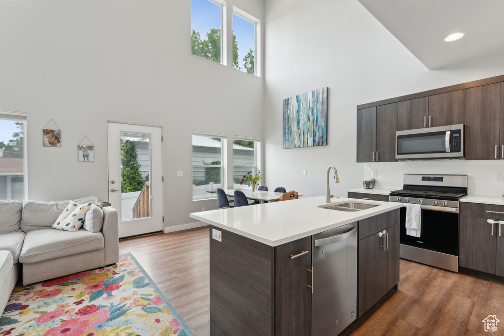 Kitchen featuring appliances with stainless steel finishes, a sink, a towering ceiling, light countertops, and open floor plan