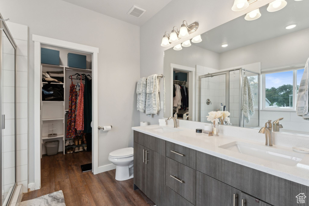 Full bathroom with a stall shower, wood finished floors, double vanity, toilet, and baseboards