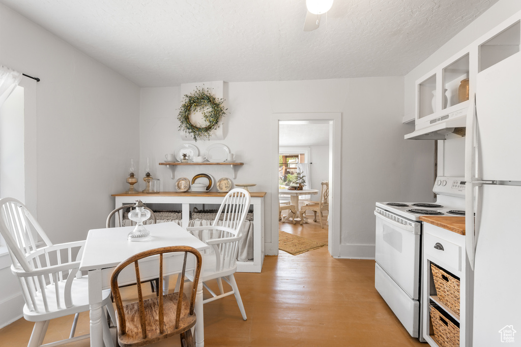 Kitchen with white appliances, under cabinet range hood, white cabinets, light wood-style floors, and glass insert cabinets