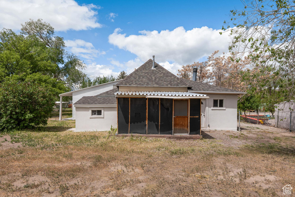 Back of house with a sunroom, roof with shingles, fence, and stucco siding