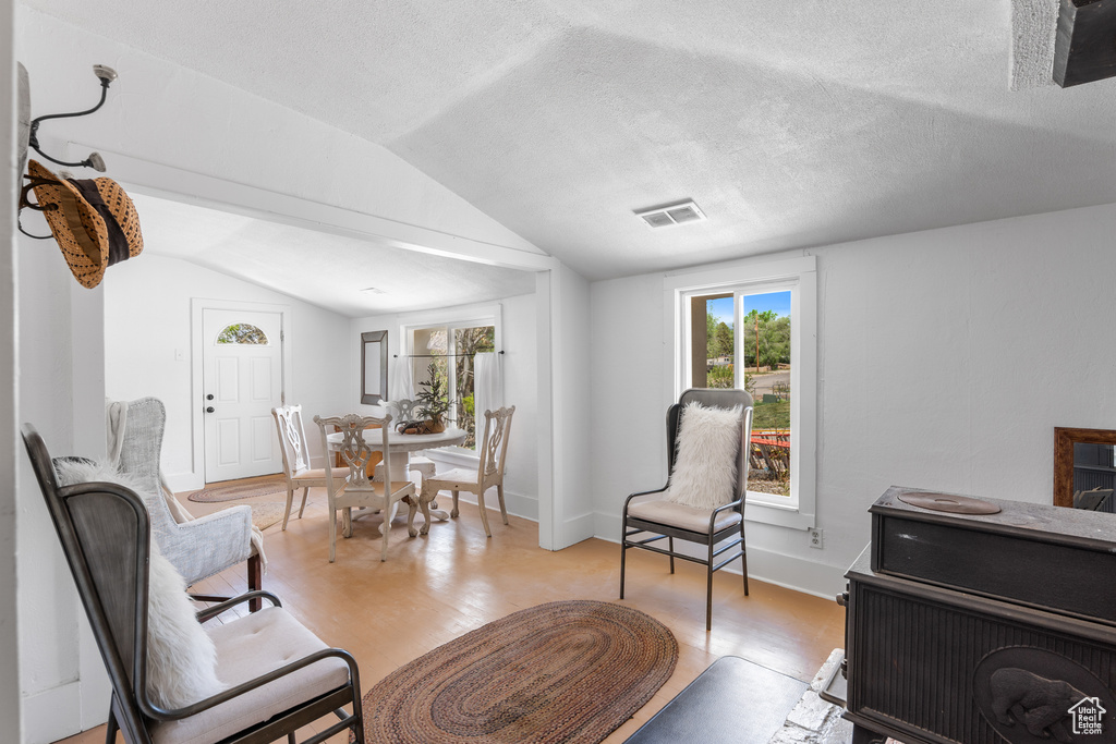 Living room with vaulted ceiling, healthy amount of natural light, light wood-style floors, a textured ceiling, and baseboards