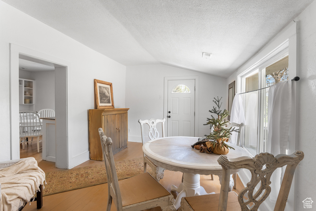 Dining area featuring vaulted ceiling, light wood finished floors, plenty of natural light, a textured ceiling, and baseboards