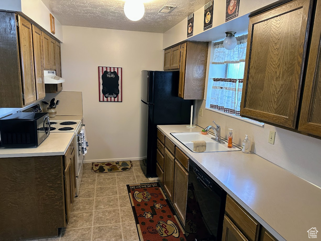 Kitchen with black appliances, a sink, ventilation hood, light countertops, and a textured ceiling