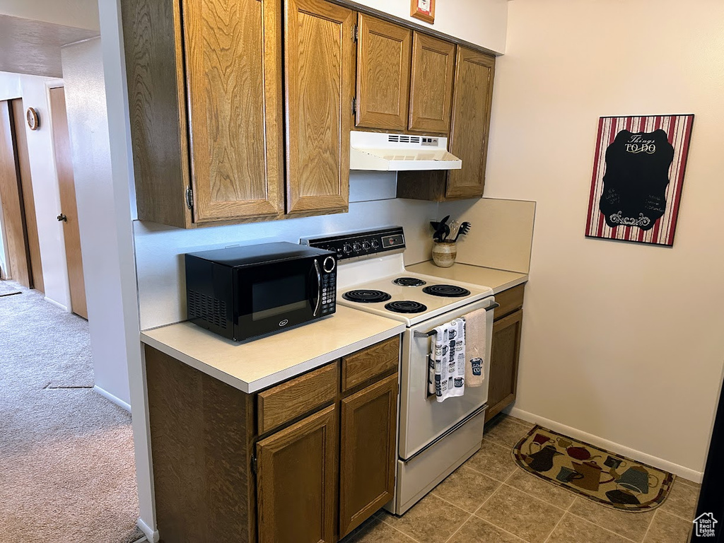Kitchen featuring under cabinet range hood, white range with electric stovetop, black microwave, light countertops, and baseboards