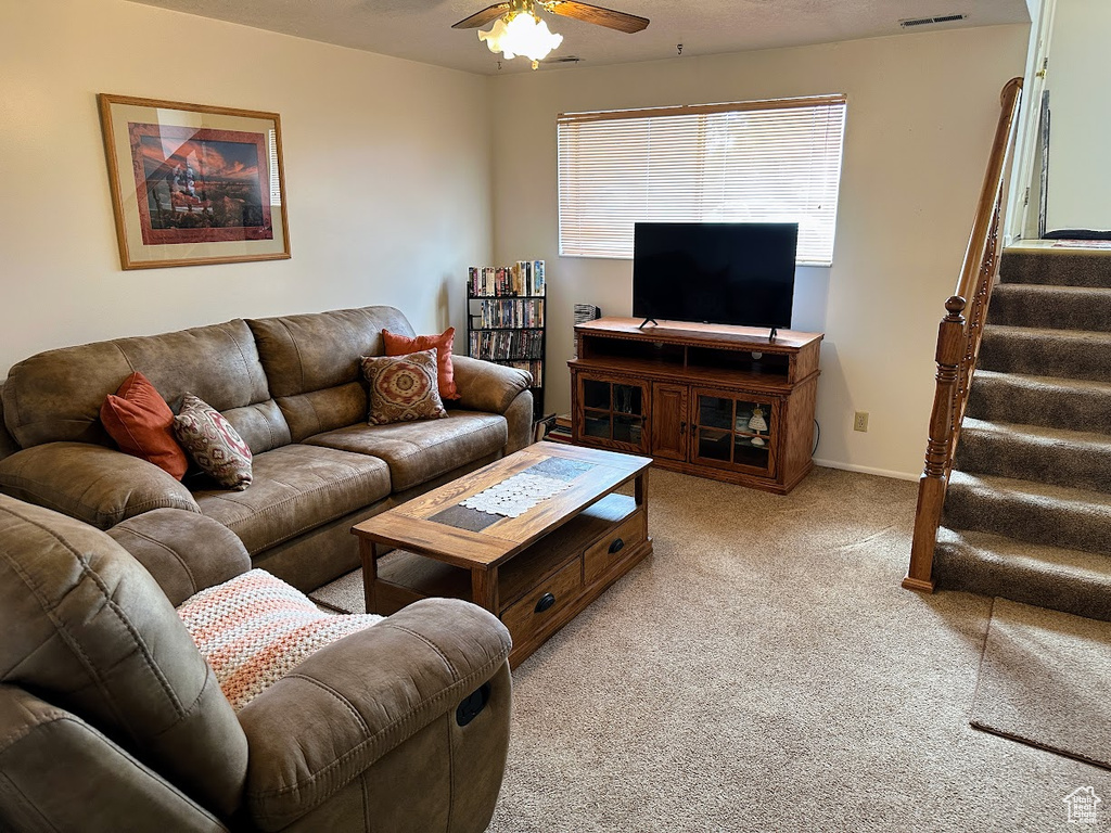 Living room featuring light carpet, ceiling fan, and stairs