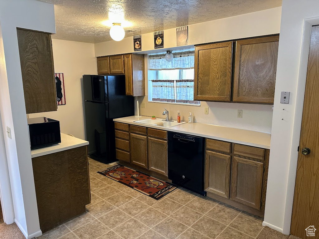 Kitchen with a sink, black appliances, a textured ceiling, and light countertops