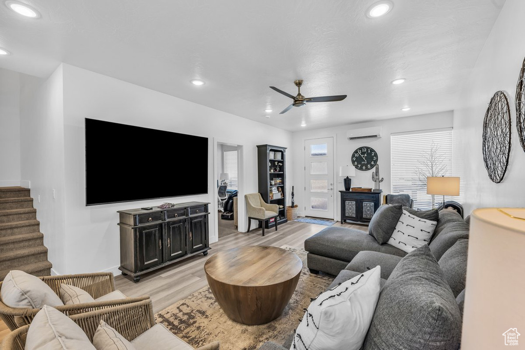 Living area with a wall unit AC, recessed lighting, light wood-type flooring, ceiling fan, and stairs