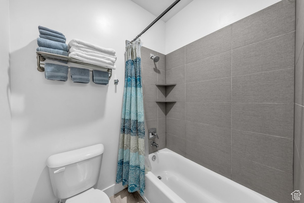 Full bath featuring shower / tub combo with curtain, toilet, and wood finished floors
