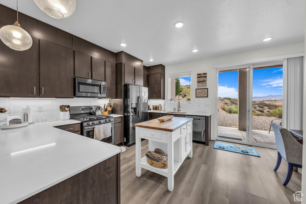 Kitchen with appliances with stainless steel finishes, dark brown cabinetry, light wood-style flooring, decorative backsplash, and wood counters