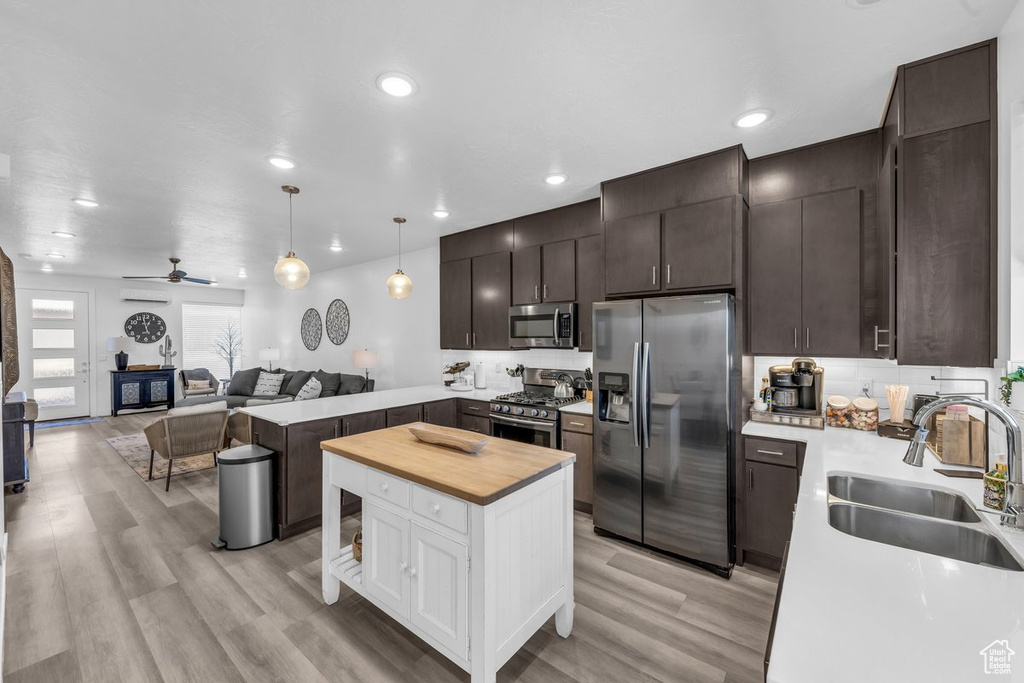 Kitchen featuring stainless steel appliances, a sink, open floor plan, butcher block counters, and dark brown cabinetry