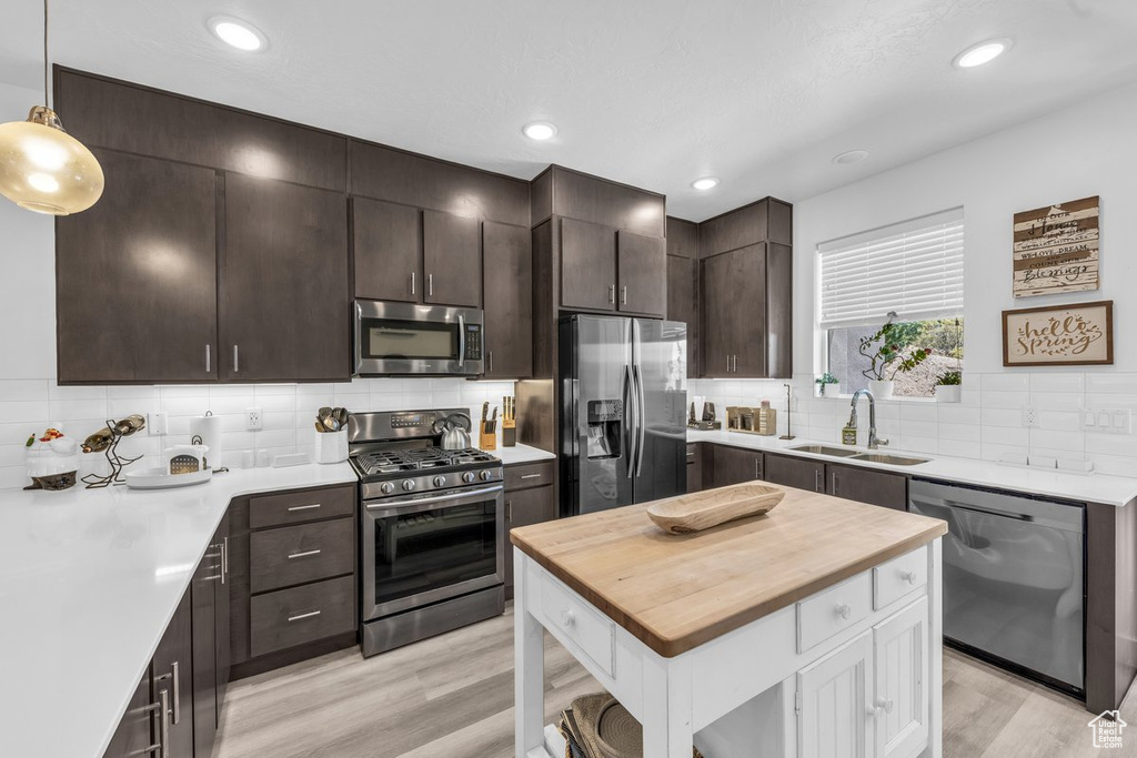 Kitchen with stainless steel appliances, a sink, butcher block counters, light wood-type flooring, and dark brown cabinetry
