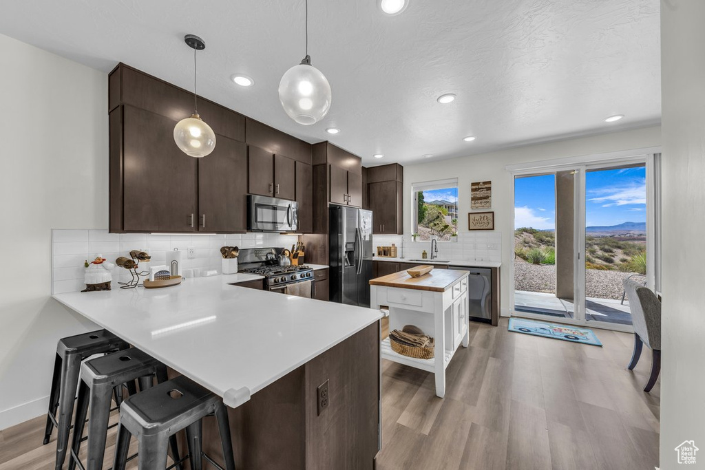 Kitchen featuring stainless steel appliances, light wood finished floors, tasteful backsplash, a breakfast bar, and a peninsula