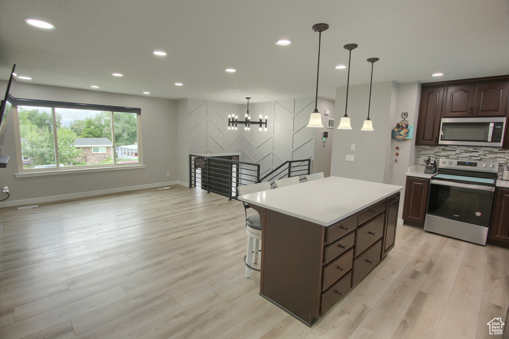 Kitchen featuring stainless steel appliances, light countertops, light wood-style flooring, decorative backsplash, and dark brown cabinetry
