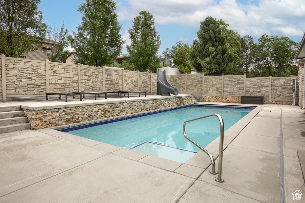 View of swimming pool with a water slide, a fenced backyard, and a patio
