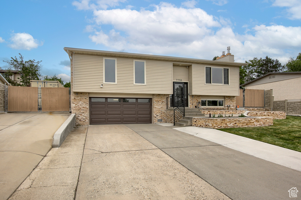 Bi-level home with an attached garage, fence, driveway, and a chimney