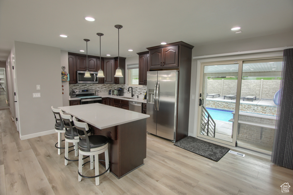 Kitchen with appliances with stainless steel finishes, dark brown cabinetry, light wood-type flooring, light countertops, and recessed lighting