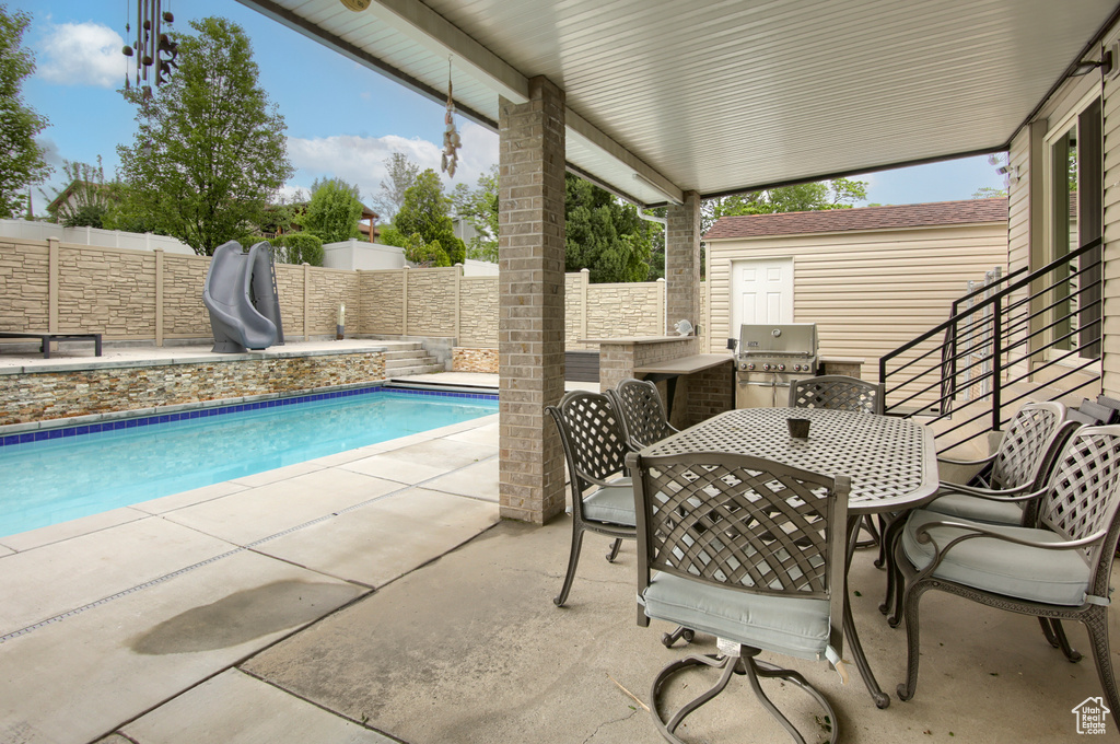 View of swimming pool with a water slide, a fenced backyard, a patio area, and area for grilling