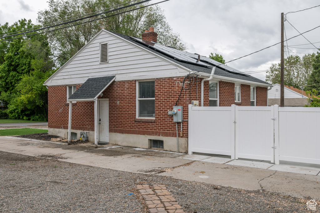 View of side of home with a gate, a chimney, brick siding, and solar panels