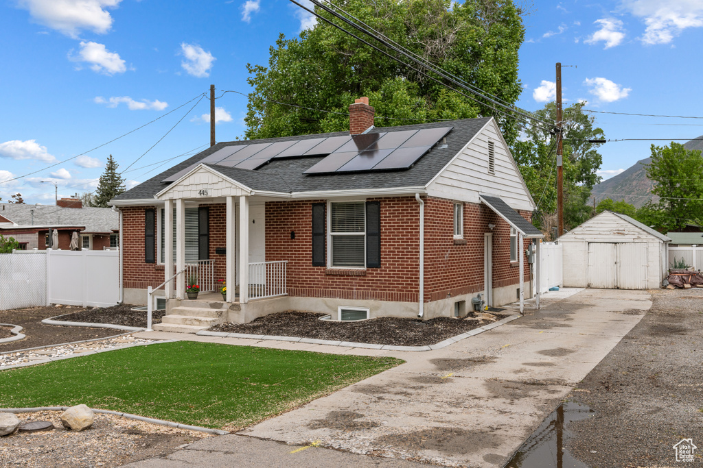 View of front facade featuring a chimney, brick siding, roof mounted solar panels, and a shingled roof