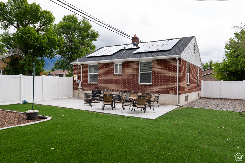Back of property with brick siding, roof mounted solar panels, and a patio