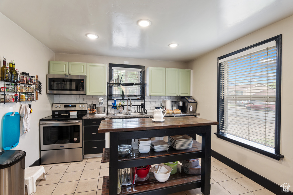 Kitchen with appliances with stainless steel finishes, green cabinetry, a sink, light tile patterned flooring, and backsplash