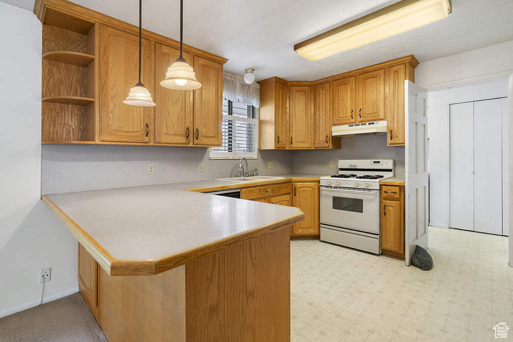 Kitchen featuring white gas range, under cabinet range hood, a sink, light countertops, and a peninsula