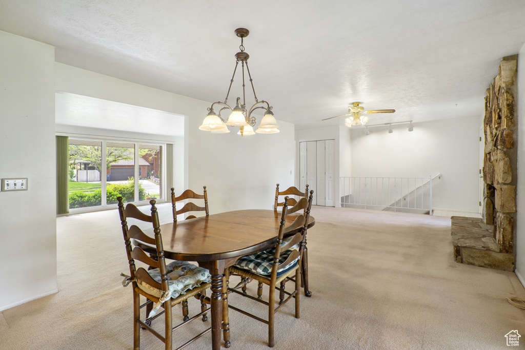 Dining space with light colored carpet, a ceiling fan, track lighting, and a chandelier