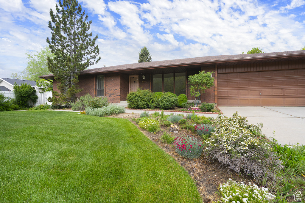 View of front of home featuring driveway, brick siding, an attached garage, and a front lawn