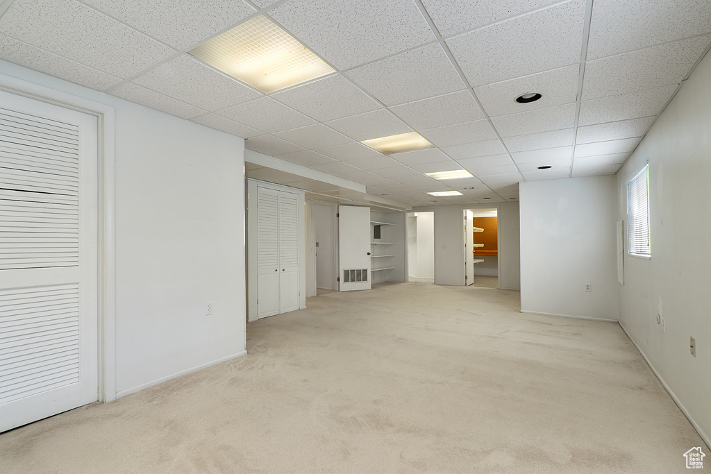 Basement featuring a drop ceiling, light carpet, and baseboards