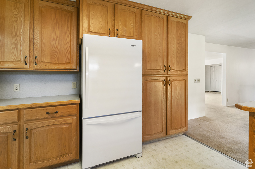 Kitchen with freestanding refrigerator, light floors, light countertops, and brown cabinetry