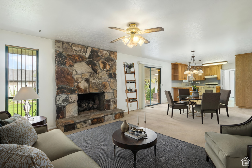 Living area with a ceiling fan, light carpet, a chandelier, and a stone fireplace