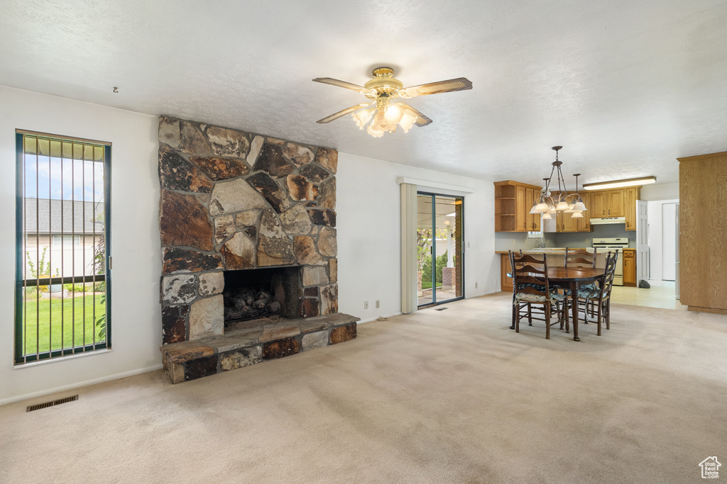 Living area with a chandelier, ceiling fan, a stone fireplace, light colored carpet, and a textured ceiling