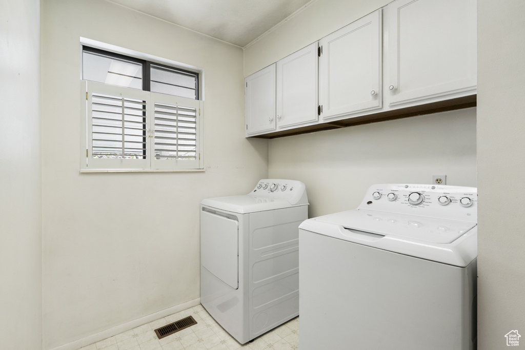 Clothes washing area featuring washer and clothes dryer, cabinet space, light floors, and baseboards