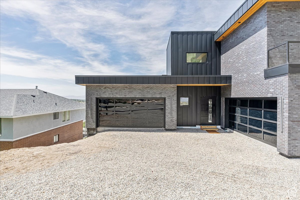 View of front of house with board and batten siding, driveway, an attached garage, and brick siding