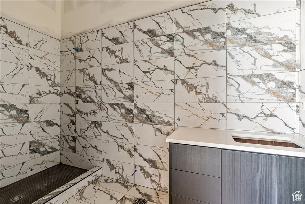 Bathroom featuring tiled shower, marble finish flooring, and tile walls