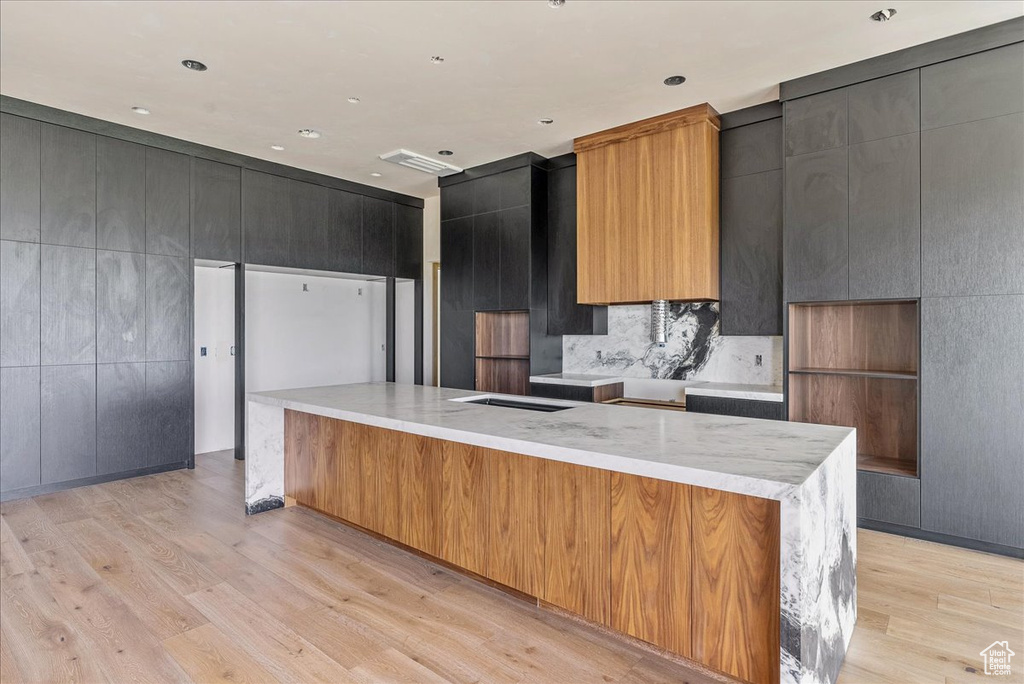 Kitchen featuring light wood-style flooring, a large island, modern cabinets, decorative backsplash, and light stone countertops