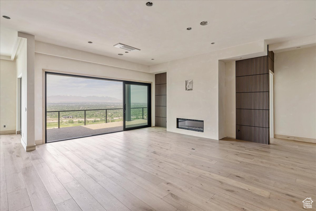 Unfurnished living room featuring light wood finished floors, a glass covered fireplace, baseboards, and recessed lighting