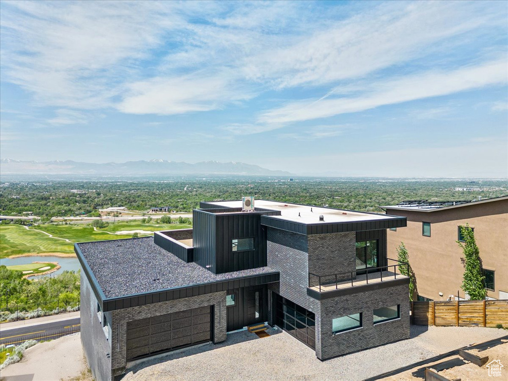 Contemporary house featuring a mountain view, a balcony, gravel driveway, and a garage
