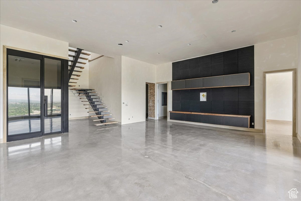 Unfurnished living room with concrete floors, a high ceiling, and stairway