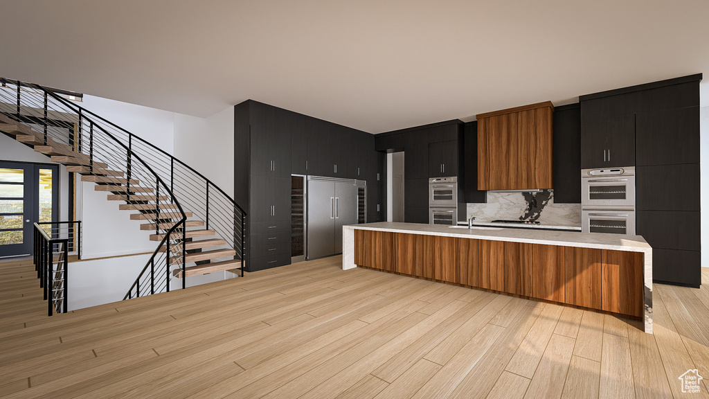 Kitchen featuring light countertops, light wood-style floors, appliances with stainless steel finishes, dark cabinetry, and a large island