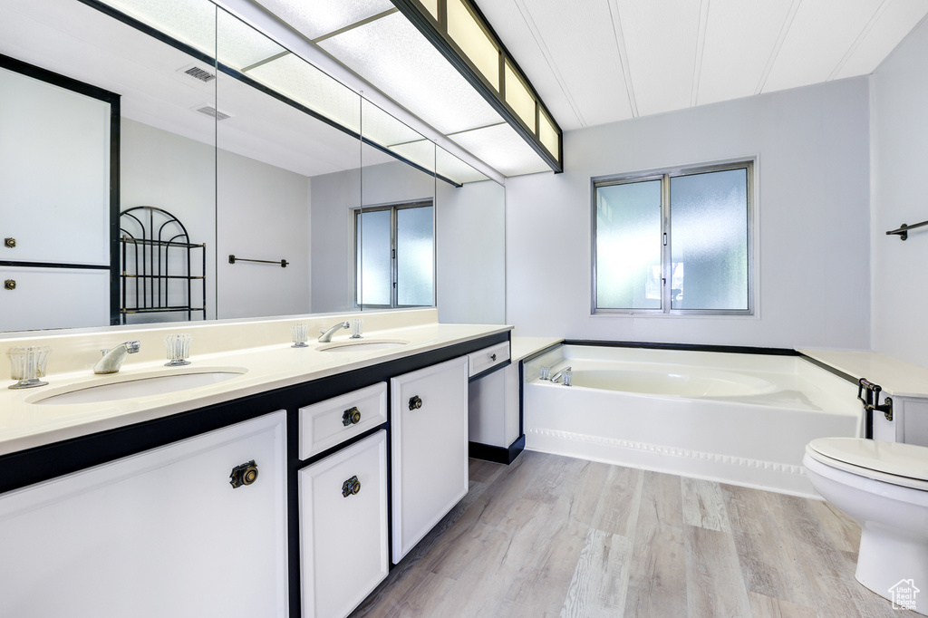 Bathroom with wood finished floors, a garden tub, double vanity, and toilet