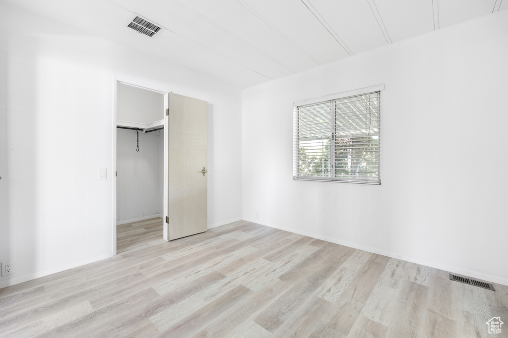 Unfurnished bedroom with light wood-style floors, a closet, a spacious closet, and baseboards