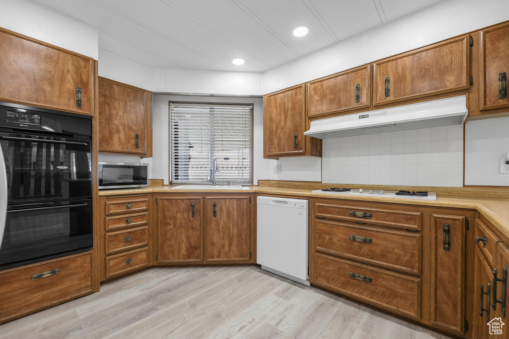 Kitchen with white appliances, under cabinet range hood, a sink, brown cabinetry, and backsplash