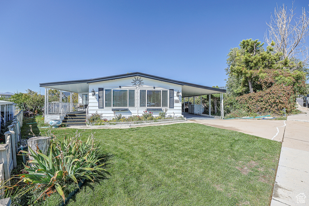 Manufactured / mobile home featuring an attached carport, a front lawn, concrete driveway, and covered porch