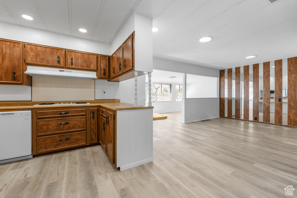 Kitchen with white appliances, under cabinet range hood, open floor plan, brown cabinetry, and light wood-style floors