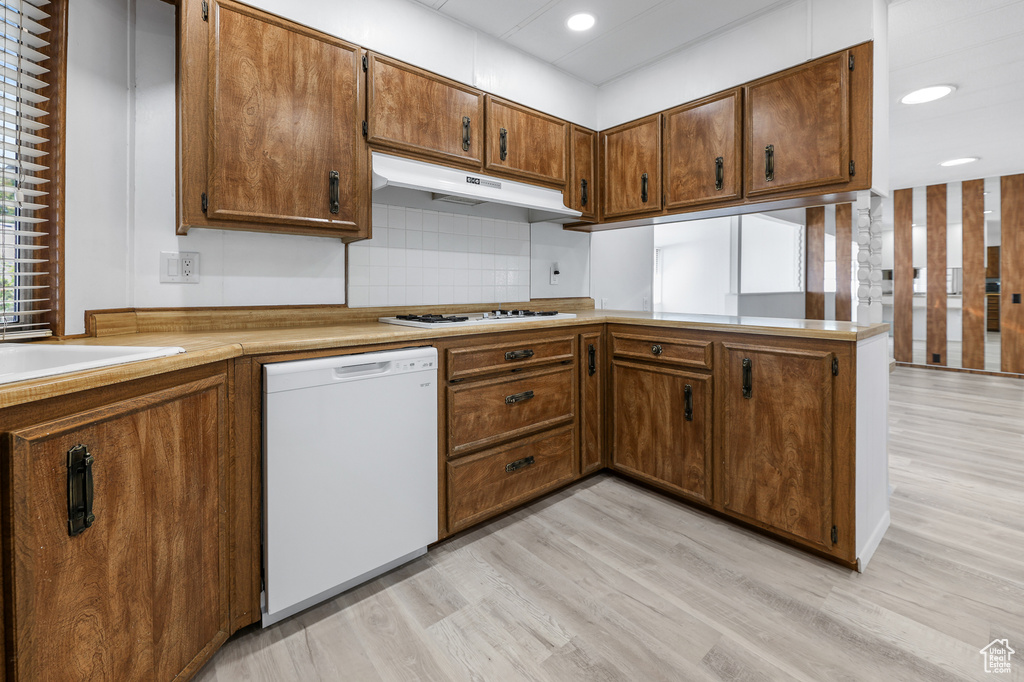 Kitchen featuring white appliances, under cabinet range hood, decorative backsplash, light wood-type flooring, and recessed lighting