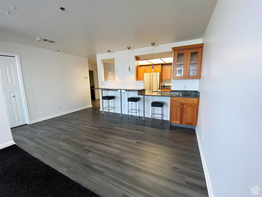 Kitchen featuring brown cabinetry, dark wood-style floors, a kitchen breakfast bar, refrigerator, and glass insert cabinets