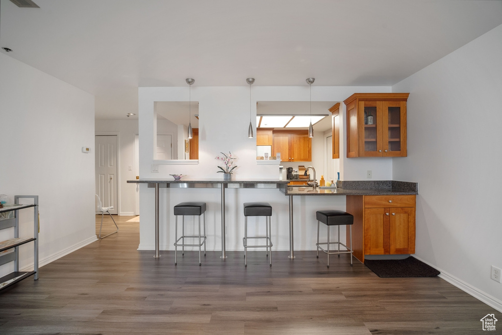Kitchen featuring brown cabinets, glass insert cabinets, a kitchen bar, dark wood-style flooring, and a peninsula